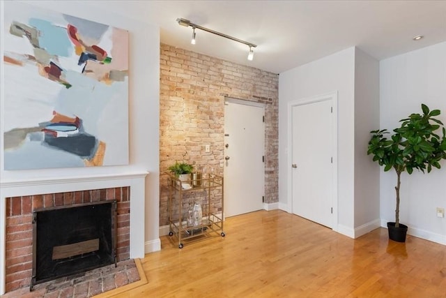 living room with a brick fireplace, rail lighting, wood finished floors, and baseboards