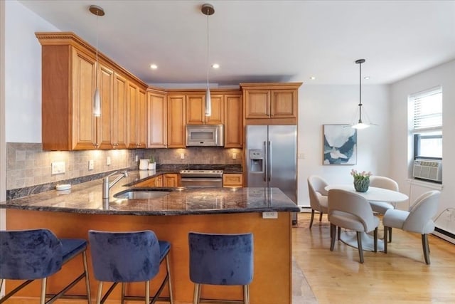 kitchen featuring dark stone counters, brown cabinets, appliances with stainless steel finishes, a peninsula, and a sink