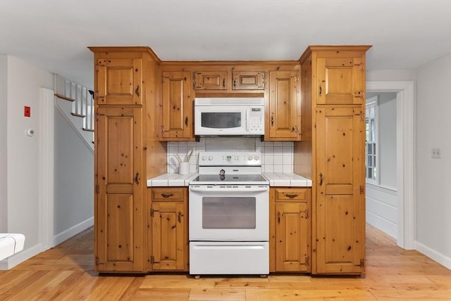 kitchen featuring white appliances, tile countertops, light wood-type flooring, and decorative backsplash