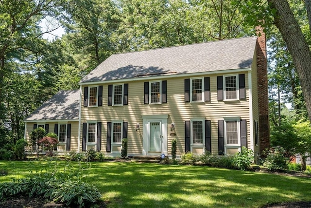 colonial-style house featuring a front yard, roof with shingles, and a chimney