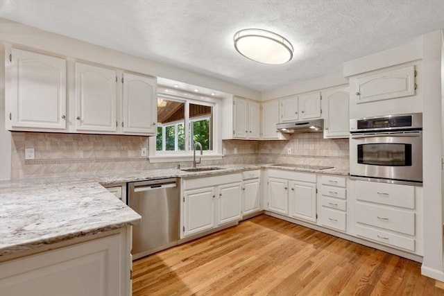 kitchen with light stone counters, appliances with stainless steel finishes, light wood-style floors, a sink, and under cabinet range hood