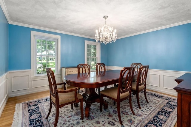 dining room featuring an inviting chandelier, light wood-style flooring, crown molding, and a wainscoted wall