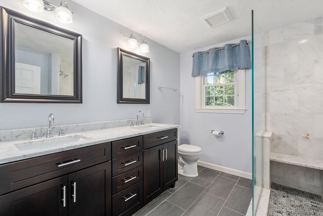 bathroom featuring a tile shower, double vanity, a sink, and toilet