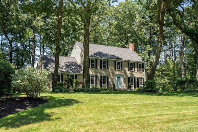 colonial home featuring a shingled roof, a front yard, and a chimney