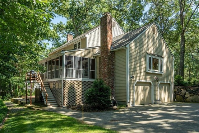 view of side of property with driveway, a sunroom, a chimney, stairway, and an attached garage