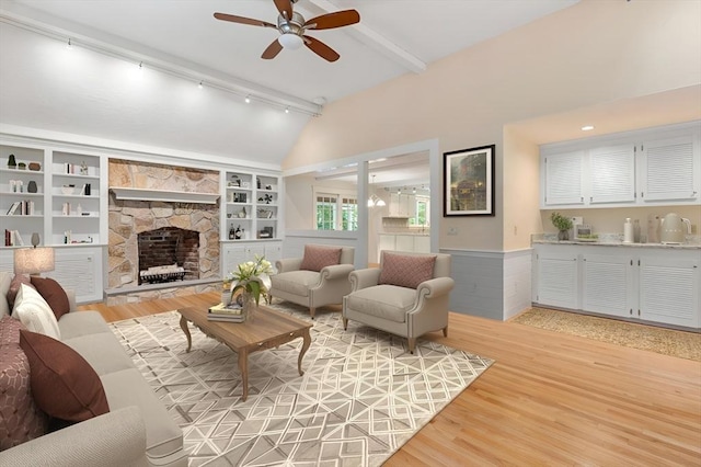 living area with lofted ceiling with beams, a stone fireplace, wood finished floors, and built in shelves