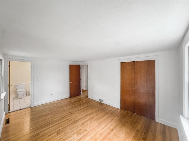 unfurnished bedroom featuring light wood-style flooring, a closet, baseboards, and connected bathroom