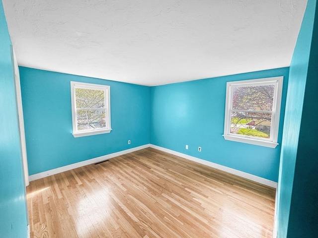 unfurnished room with a textured ceiling, wood finished floors, and baseboards