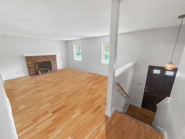 unfurnished living room featuring wood finished floors, baseboards, a textured ceiling, and a fireplace