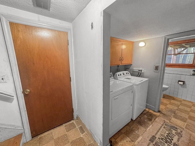 laundry area featuring a textured ceiling, independent washer and dryer, cabinet space, light flooring, and tile walls
