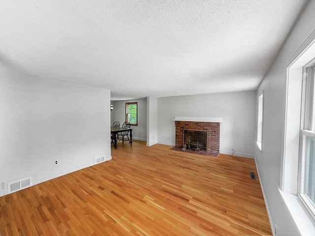 unfurnished living room with light wood-type flooring, a textured ceiling, a brick fireplace, and baseboards