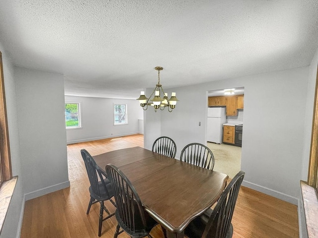 dining room featuring a chandelier, baseboards, light wood-style flooring, and a textured ceiling