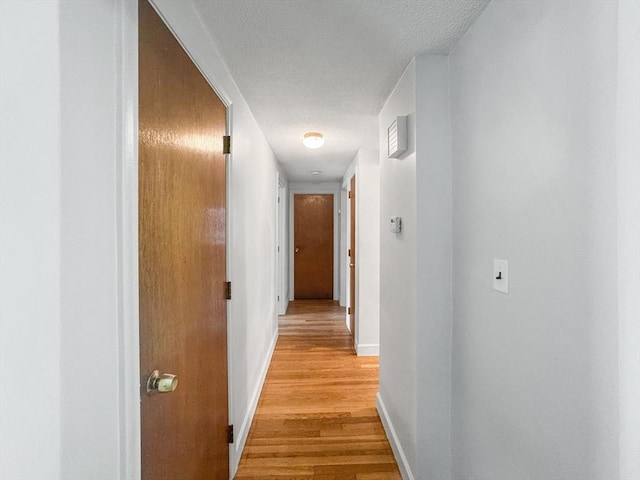 corridor with a textured ceiling, light wood-style floors, and baseboards