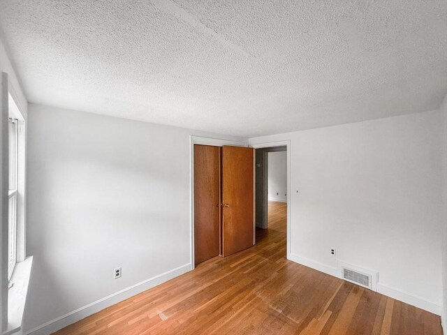 unfurnished bedroom featuring light wood-style floors, baseboards, a textured ceiling, and a closet
