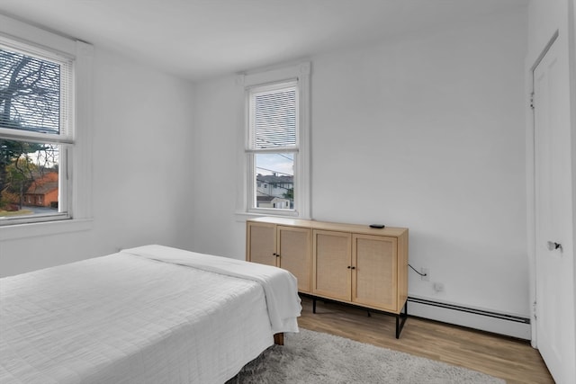 bedroom with baseboard heating, multiple windows, and light hardwood / wood-style floors