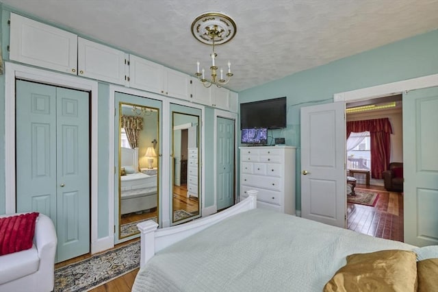 bedroom featuring a textured ceiling, wood finished floors, multiple closets, and an inviting chandelier