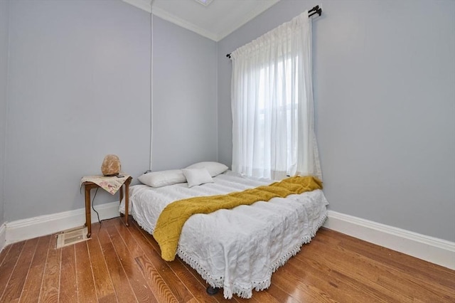 bedroom featuring wood finished floors, visible vents, crown molding, and baseboards