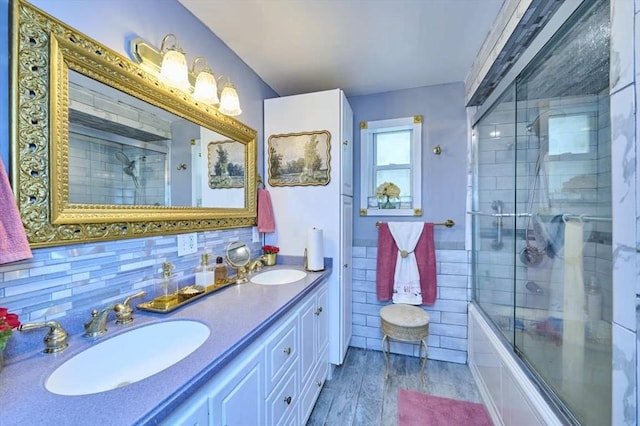 bathroom with double vanity, wood finished floors, combined bath / shower with glass door, and a sink