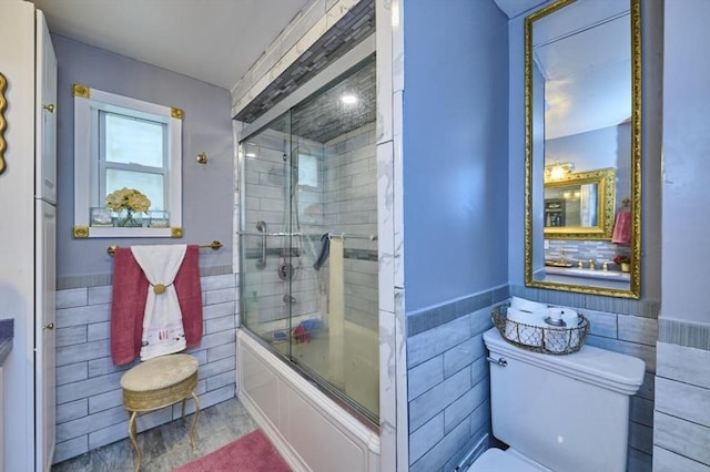 full bath featuring tile walls, combined bath / shower with glass door, a wainscoted wall, and toilet