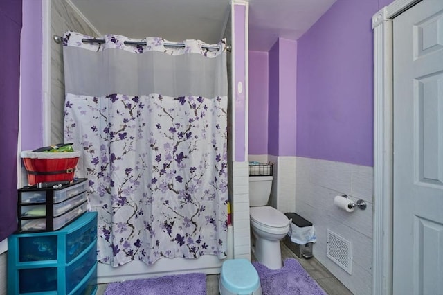 full bath with shower / bath combo, wainscoting, tile walls, toilet, and visible vents