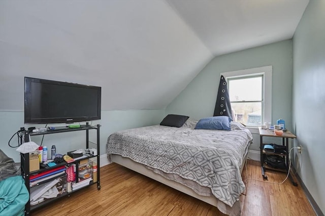 bedroom featuring lofted ceiling, baseboards, and wood finished floors