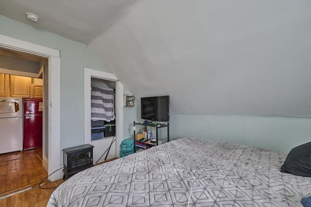 bedroom featuring lofted ceiling, a wood stove, wood finished floors, and freestanding refrigerator