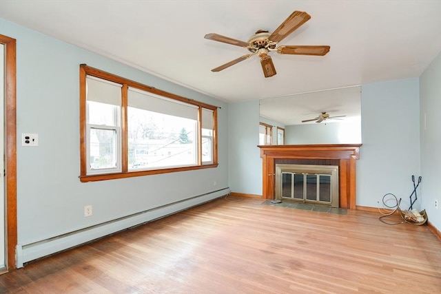 unfurnished living room featuring baseboard heating, ceiling fan, light hardwood / wood-style flooring, and a healthy amount of sunlight