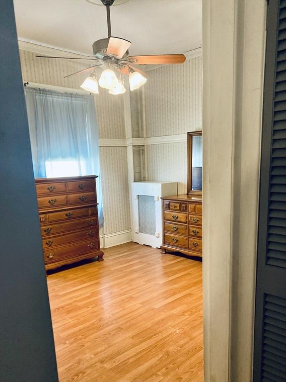 1123 S Broadway, East Providence, RI 02914 - unfurnished bedroom featuring wallpapered walls, wood finished floors, a heating unit, and a ceiling fan