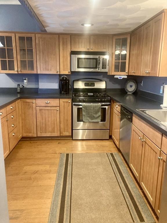 1123 S Broadway, East Providence, RI 02914 - kitchen featuring stainless steel appliances, light wood-style floors, dark countertops, and glass insert cabinets