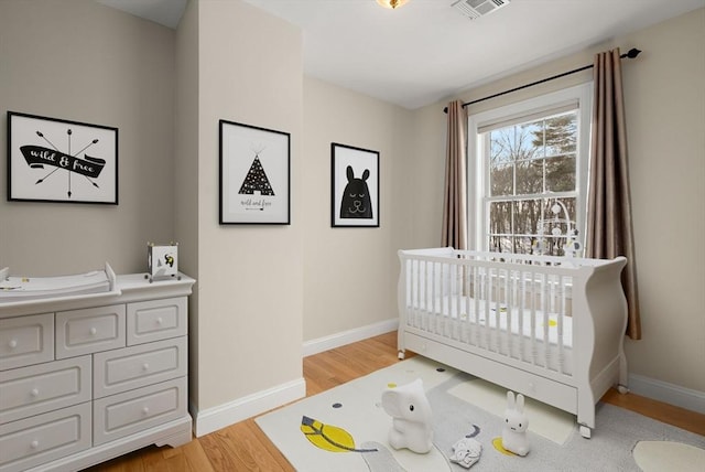 bedroom featuring a nursery area, baseboards, visible vents, and light wood-style floors