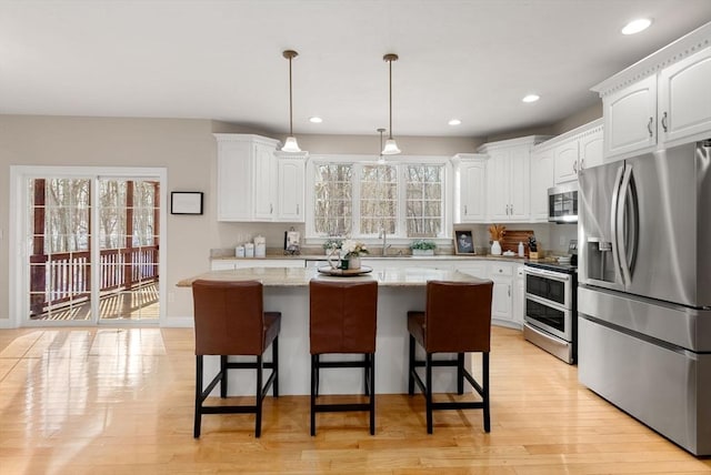 kitchen with light wood finished floors, white cabinets, a kitchen island, stainless steel appliances, and a sink