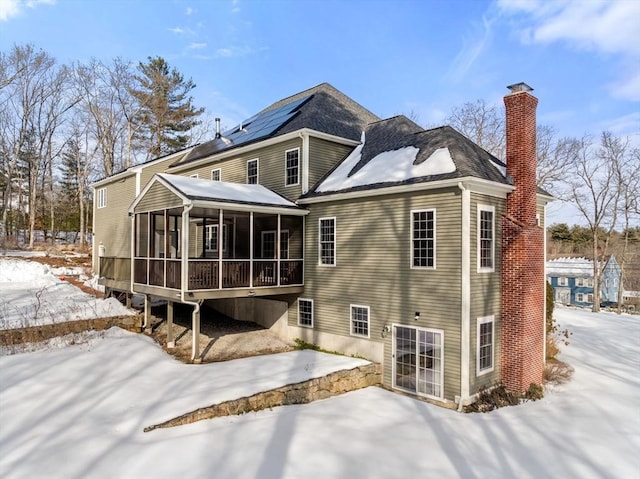 snow covered rear of property with a patio, a chimney, and a sunroom