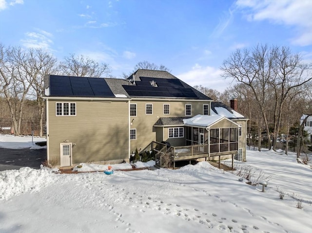 snow covered house featuring a sunroom, a wooden deck, and solar panels