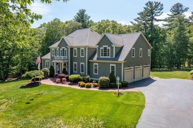 view of front of home with an attached garage, driveway, a front yard, and a balcony