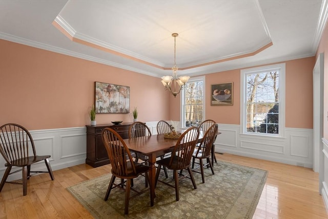 dining space with a healthy amount of sunlight, light wood-type flooring, and a raised ceiling