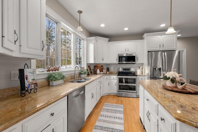 kitchen featuring stainless steel appliances, light wood-style flooring, white cabinets, a sink, and light stone countertops