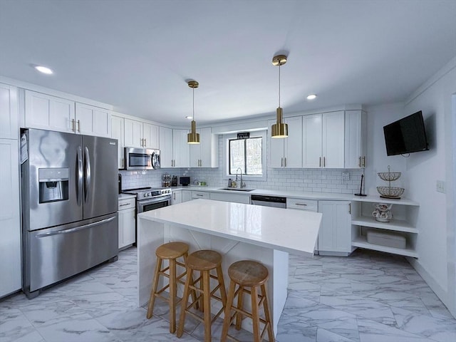 kitchen with sink, appliances with stainless steel finishes, hanging light fixtures, white cabinets, and a kitchen island