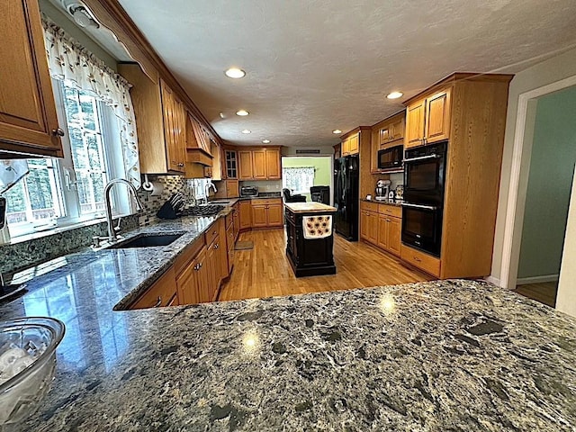 kitchen with a sink, dark stone countertops, black appliances, and a healthy amount of sunlight