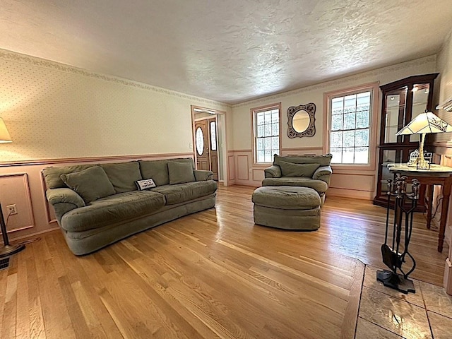 living area featuring a textured ceiling, light wood finished floors, wainscoting, and wallpapered walls