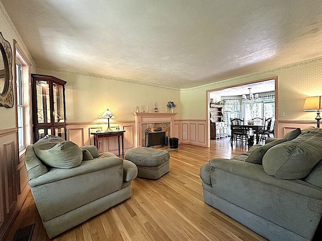 living room with wainscoting, a decorative wall, a textured ceiling, light wood-type flooring, and visible vents