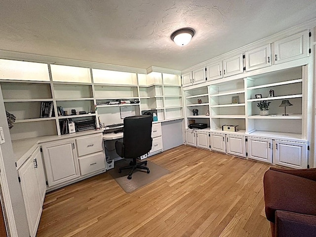 home office featuring light wood-style floors, a textured ceiling, and built in desk