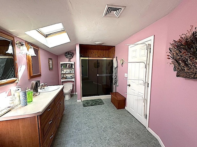 bathroom with vaulted ceiling with skylight, vanity, toilet, visible vents, and a stall shower