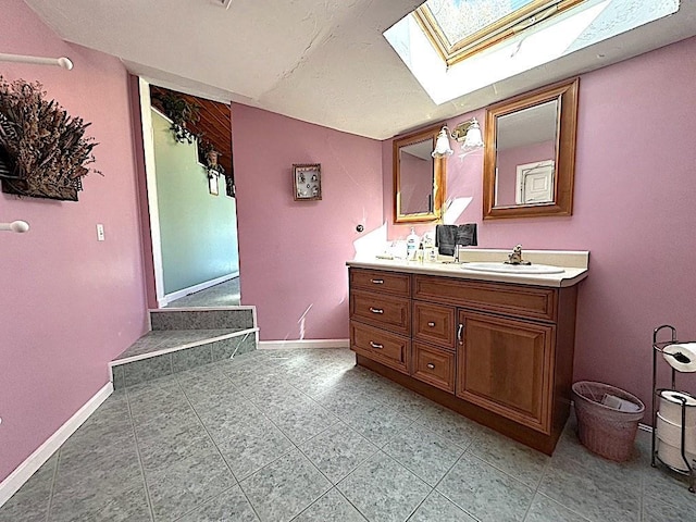 bathroom with tile patterned flooring, double vanity, baseboards, a sink, and a skylight