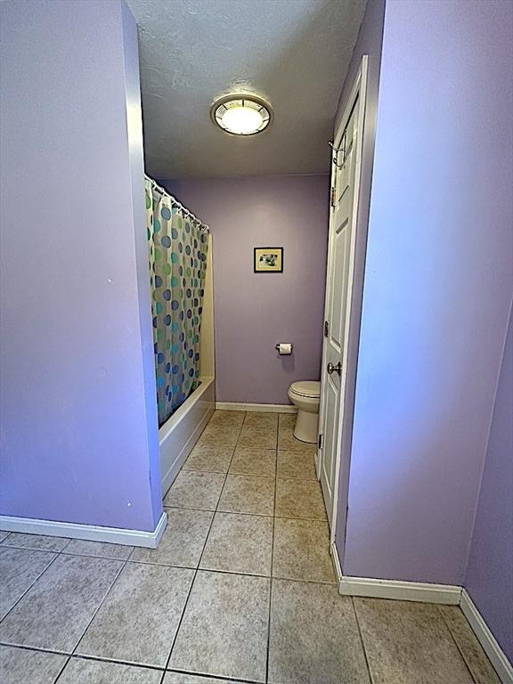bathroom featuring a textured ceiling, shower / bath combo, tile patterned floors, baseboards, and toilet