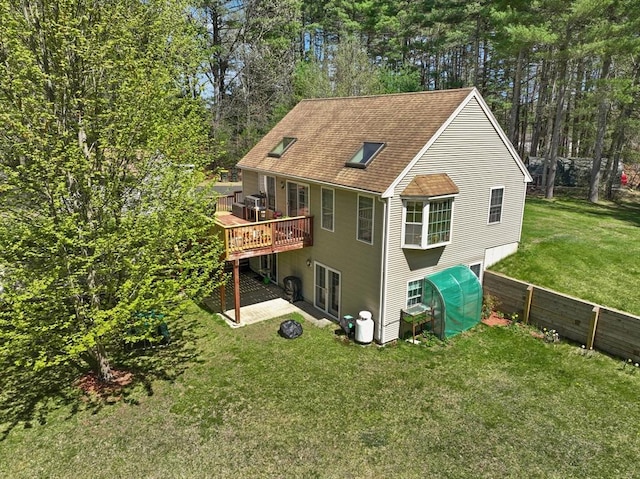 rear view of property featuring a lawn, a deck, fence, and a shingled roof