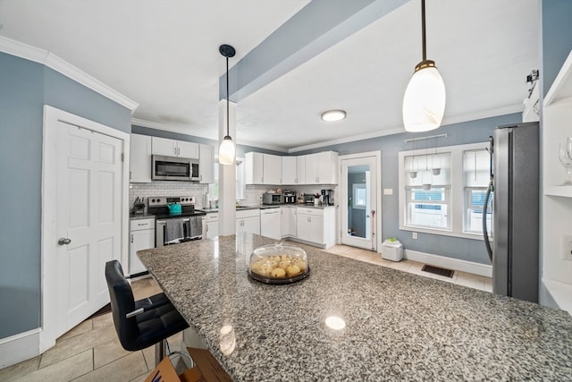 kitchen featuring white cabinetry, appliances with stainless steel finishes, dark stone countertops, a kitchen bar, and hanging light fixtures