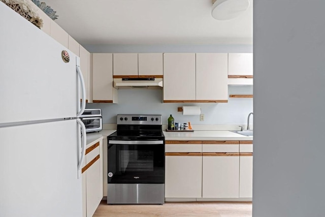 kitchen featuring freestanding refrigerator, light countertops, under cabinet range hood, and stainless steel electric range