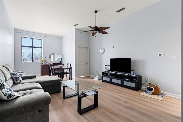 living room featuring baseboards, visible vents, light wood-style floors, and a ceiling fan