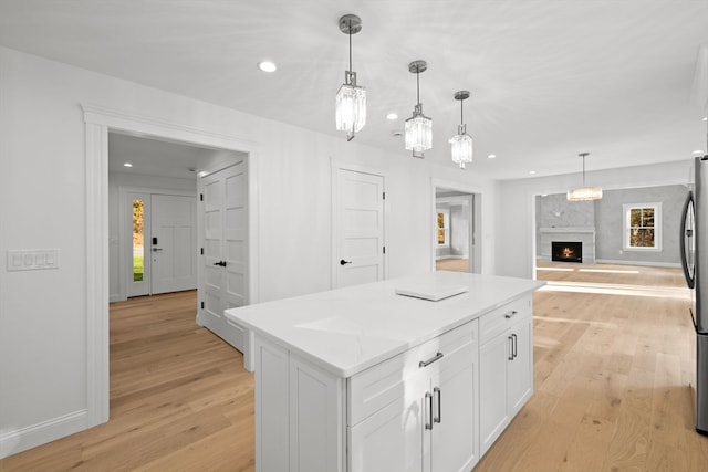 kitchen featuring white cabinets, a kitchen island, light wood-type flooring, and a fireplace