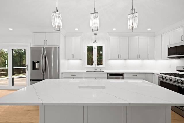 kitchen with appliances with stainless steel finishes, sink, light hardwood / wood-style flooring, white cabinets, and hanging light fixtures